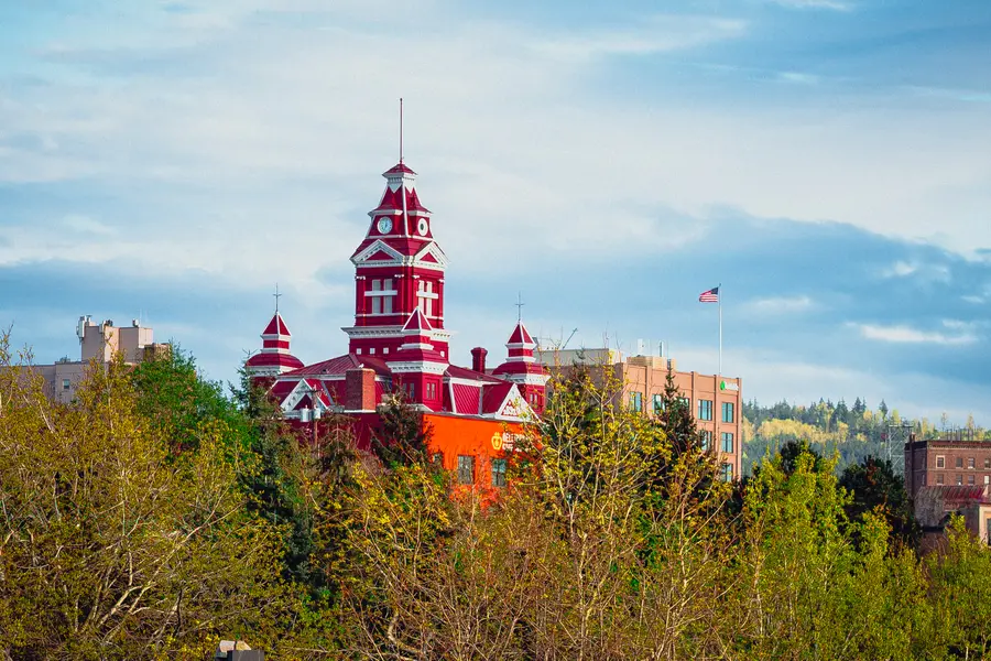 A red brick clocktower rising above fresh spring trees against a pale blue sky.