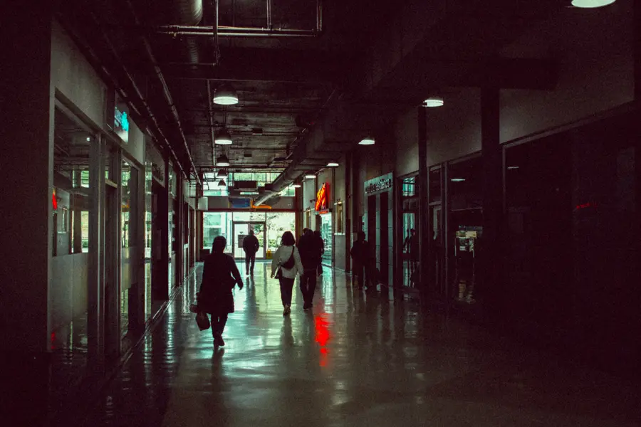 Silhouetted people walking through a dim corridor with a red neon reflection on the floor.